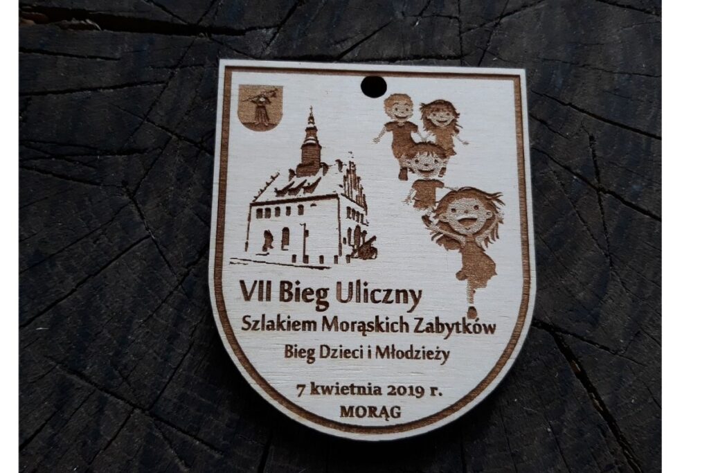 Drewniany medal dla dzieci na VII Bieg Uliczny w Morasku, grawerowany laserowo z motywem zabytkowego kościoła.