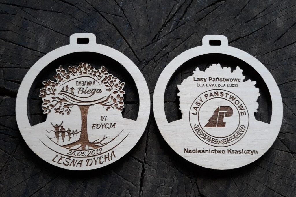 Drewniany medal ażurowy na bieg Dybawka Biega 2019, okrągły, wycinany laserowo z motywem drzewa.