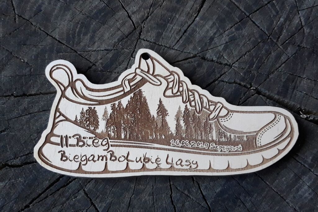 Drewniany medal w kształcie buta do biegania z wygrawerowanym logo II Biegu BiegamBoLubie Lasy i sylwetkami drzew.