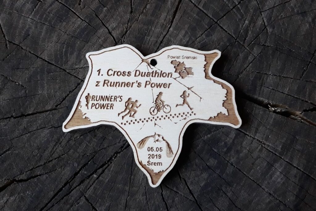 Drewniany medal w kształcie liścia klonu z wygrawerowaną postacią biegacza i kolarza oraz napisem Duathlon.