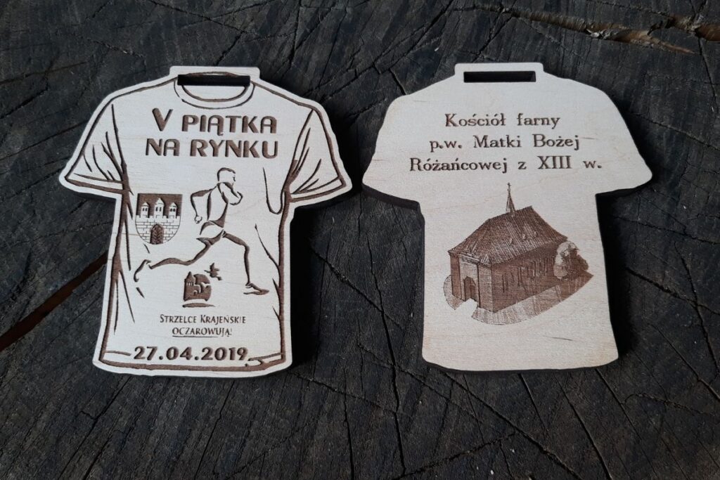 Drewniany medal w kształcie koszulki biegowej z wygrawerowanym numerem 5, nazwą biegu V Piątka na Rynku i wygrawerowanym na rewersie zdjęciem Kościoła.