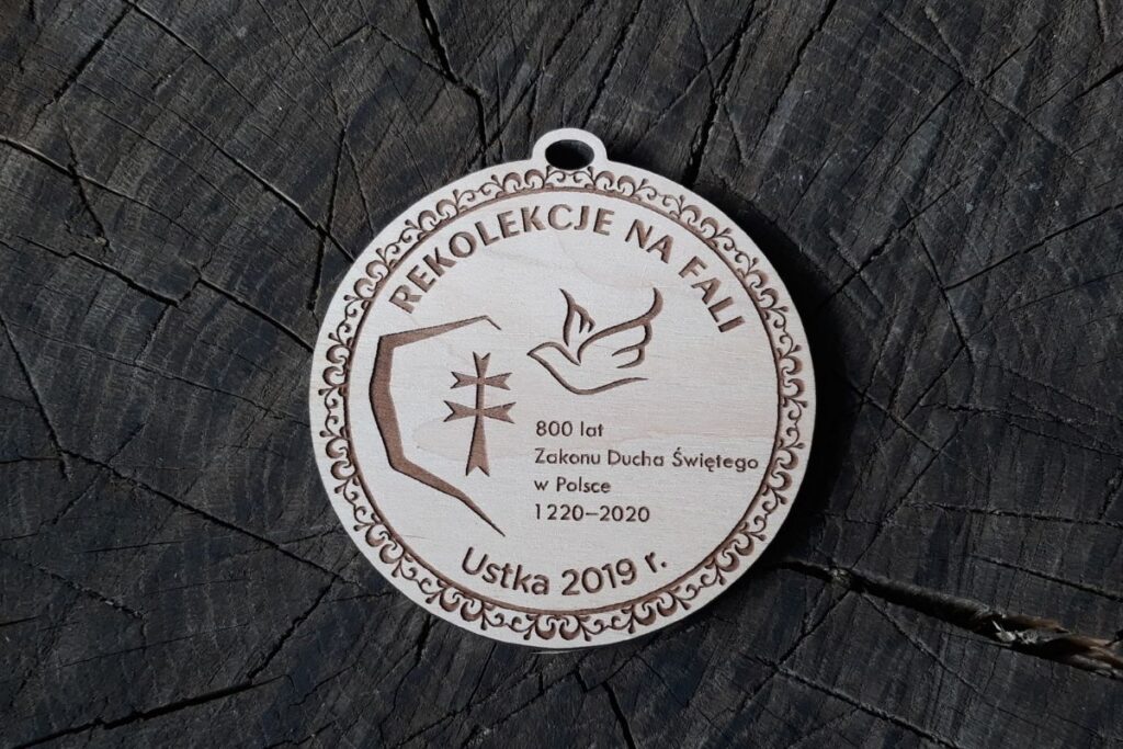 Pamiątkowy medal z jasnego drewna z laserowym grawerem maryjnym i ozdobnym motywem, pamiątka wydarzenia religijnego w Ustce.