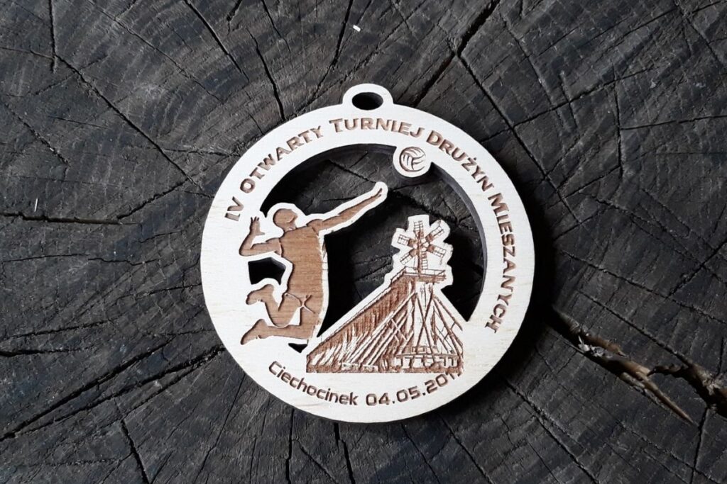 Okrągły drewniany medal ażurowy z wyciętym motywem siatkarza uderzającego piłkę nad siatką.