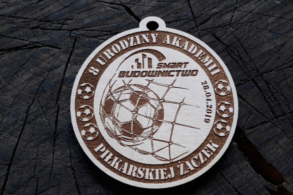 Okrągły drewniany medal urodzinowy Akademii z wygrawerowaną piłką siatkową, napisem Urodziny Akademii zawieszeniem na sznurek.