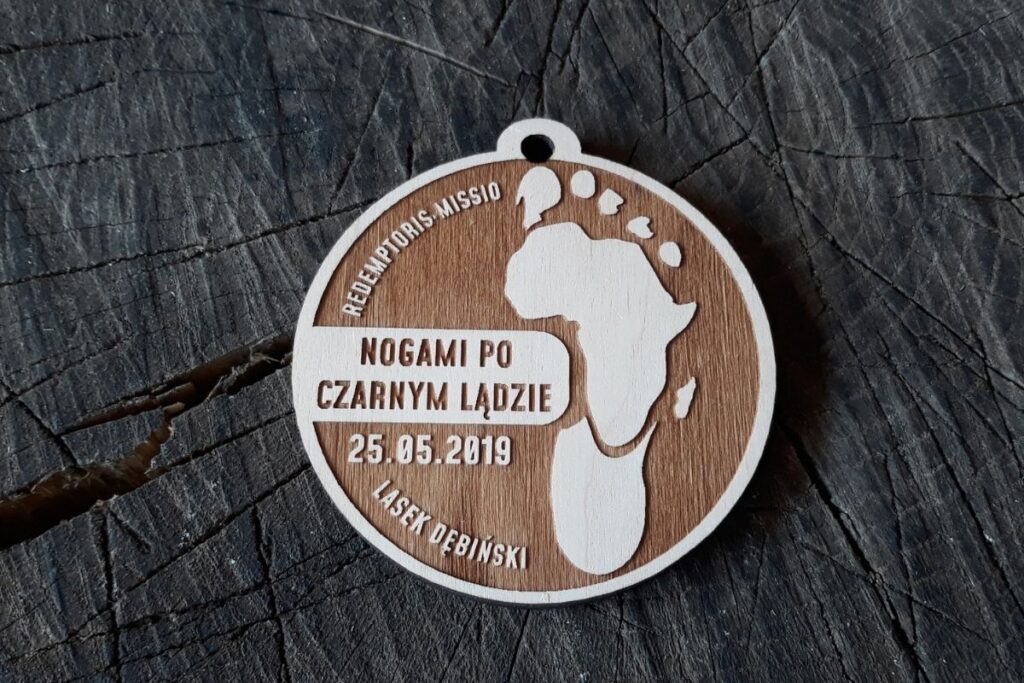 Okrągły drewniany medal z grawerowaną mapą Afryki w kształcie stopy oraz napisem Nogami po Czarnym Lądzie.