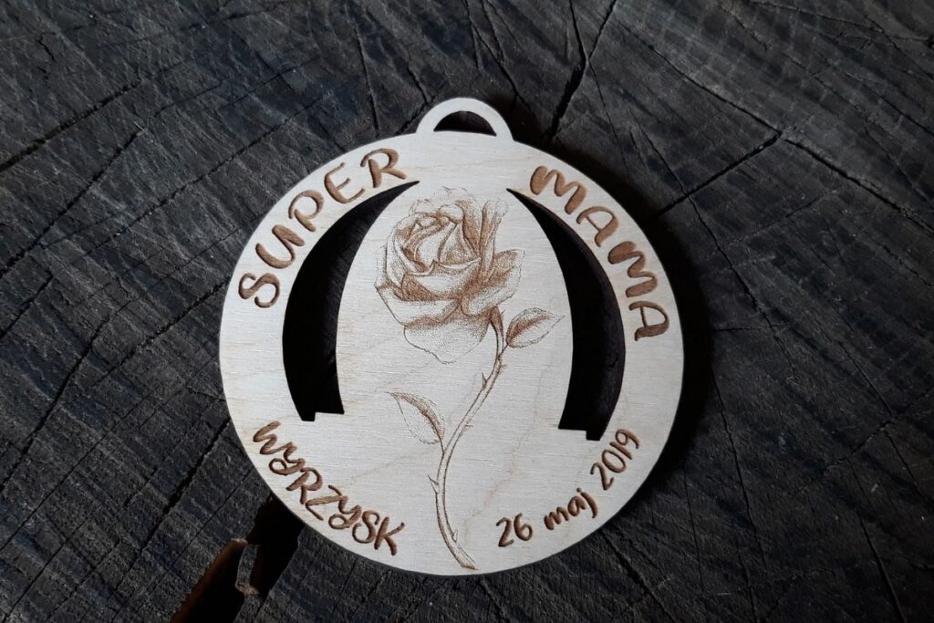 Okrągły drewniany medal z grawerowanym napisem 'Dla Super Mamy', ozdobiony motywem ażurowym z różą.