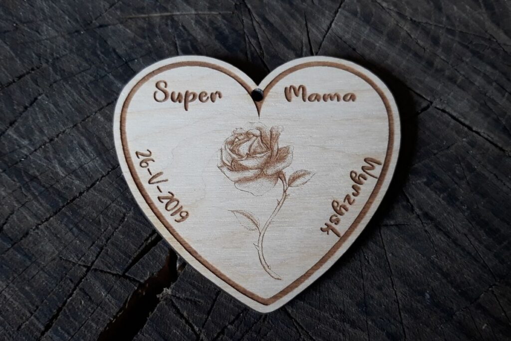 Drewniany medal w kształcie serca z wygrawerowaną różą, napisem 'Super Mama'.