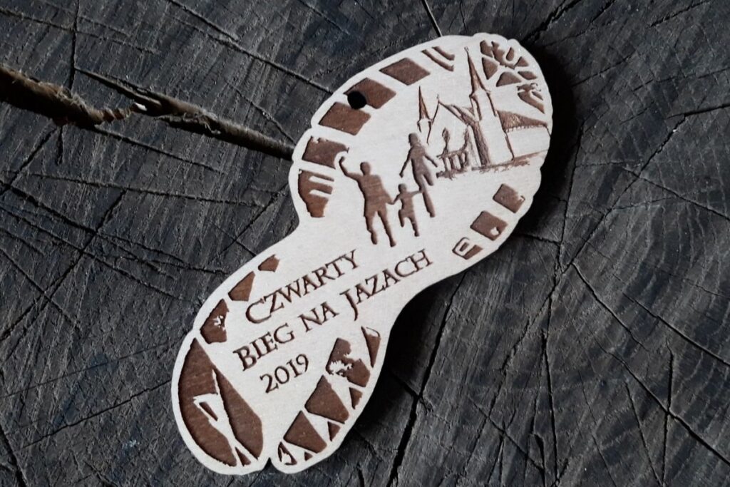 Drewniany medal w kształcie podeszwy buta sportowego z wyraźnym grawerem bieżnika, sylwetką biegacza i miejscem na nazwę zawodów