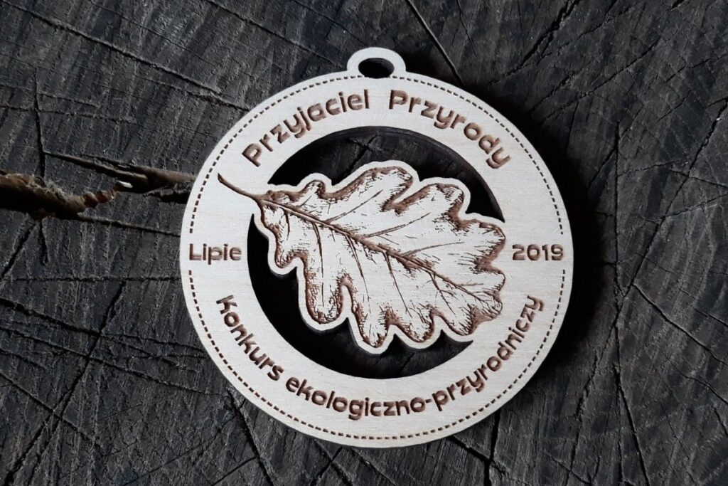 Okrągły drewniany medal z wyciętym ażurowo kształtem liścia dębu, napisem Przyjaciel Przyrody i grawerowanymi detalami.