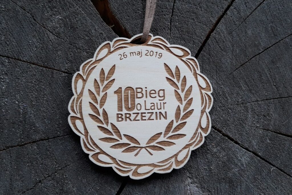 Okrągły drewniany medal z grawerowanym wieńcem laurowym otaczającym miejsce na personalizowany napis lub logo