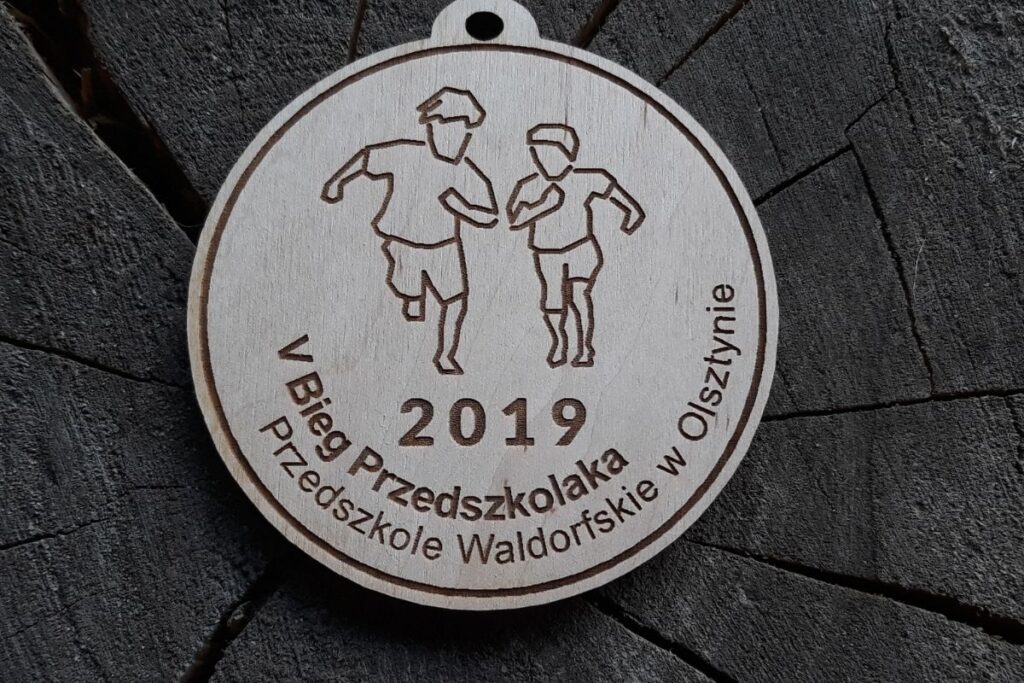 Okrągły drewniany medal na Biegi Przedszkolaka z grawerem zarysu dzieci, oraz napisem Biegi Przedszkolaka.