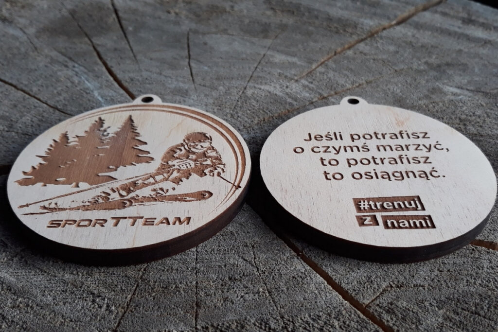 Okrągły drewniany medal z grawerem narciarza w dynamicznym zjeździe, z motywującym cytatem.