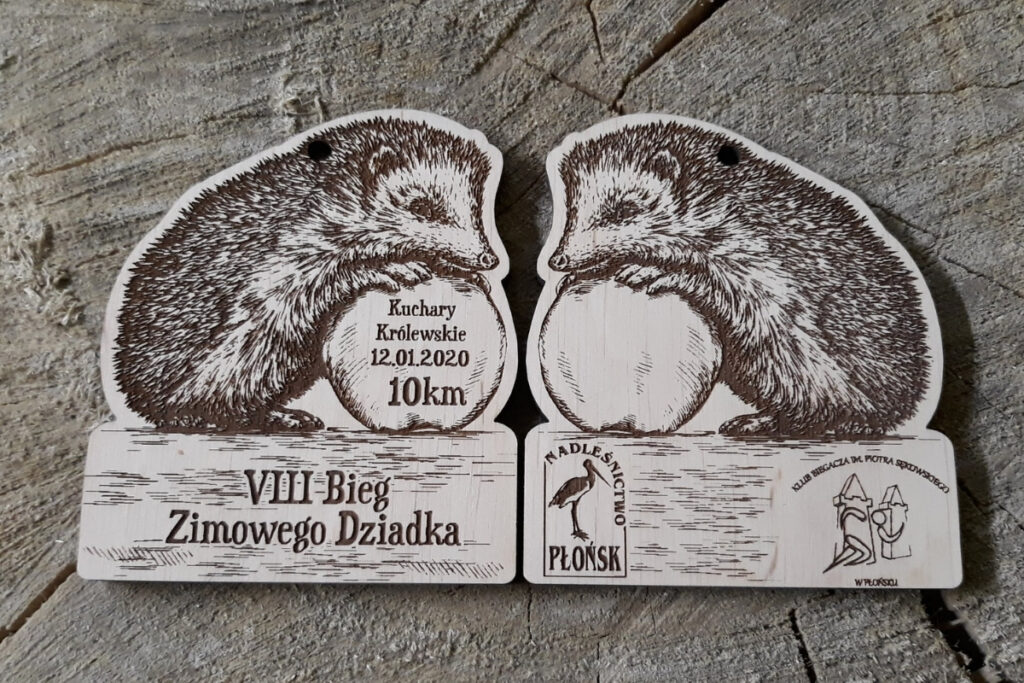 Drewniany medal wycięty w kształcie jeża z wygrawerowanymi kolcami, małym noskiem i napisami oraz logiem na dole.