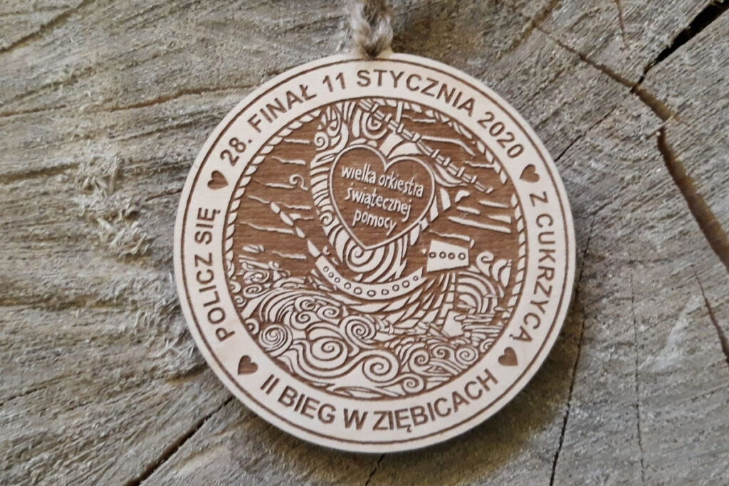 Okrągły drewniany medal z grawerowanym  sercem WOŚP, napisem 28. Finał oraz nazwą biegu i miejsca.