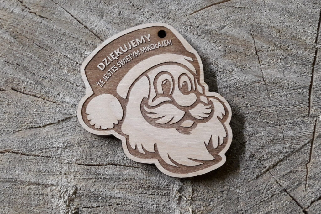 Drewniany medal wycięty w kształcie głowy św. Mikołaja z charakterystyczną czapką i brodą, z grawerem podziękowania za udział w akcji charytatywnej.