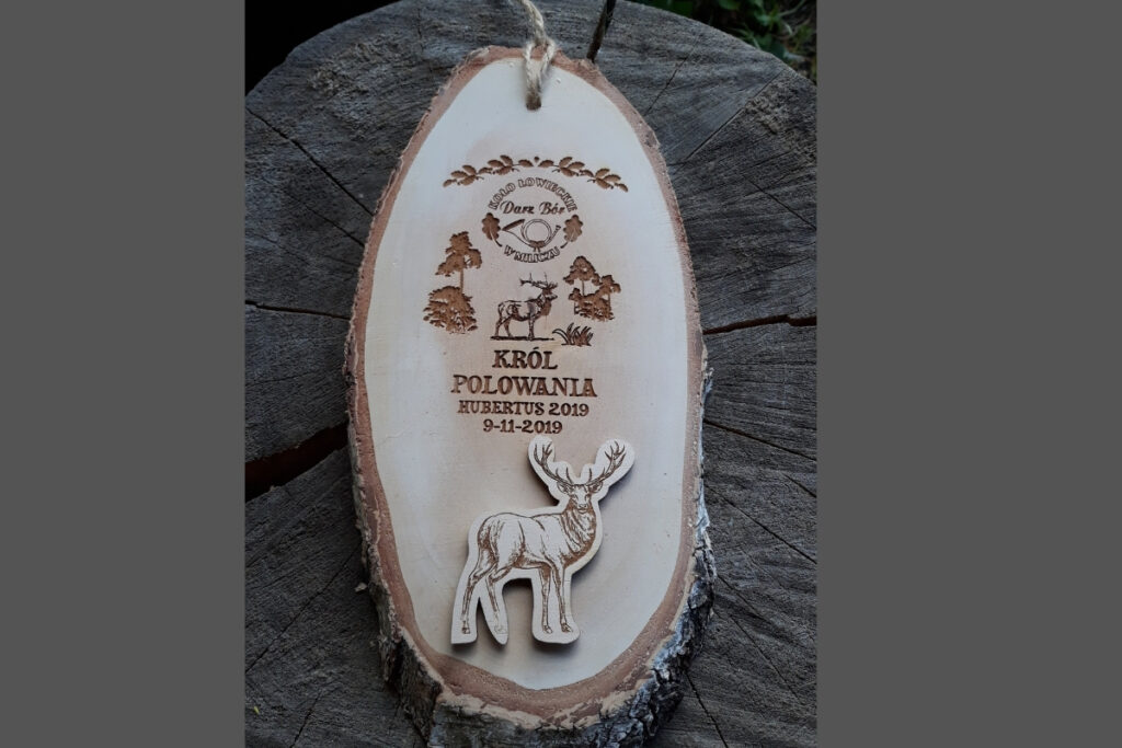 Duży medal myśliwski wykonany z grubego, skośnie ciętego plastra brzozy z korą, z grawerem jelenia i napisem Król Polowania.