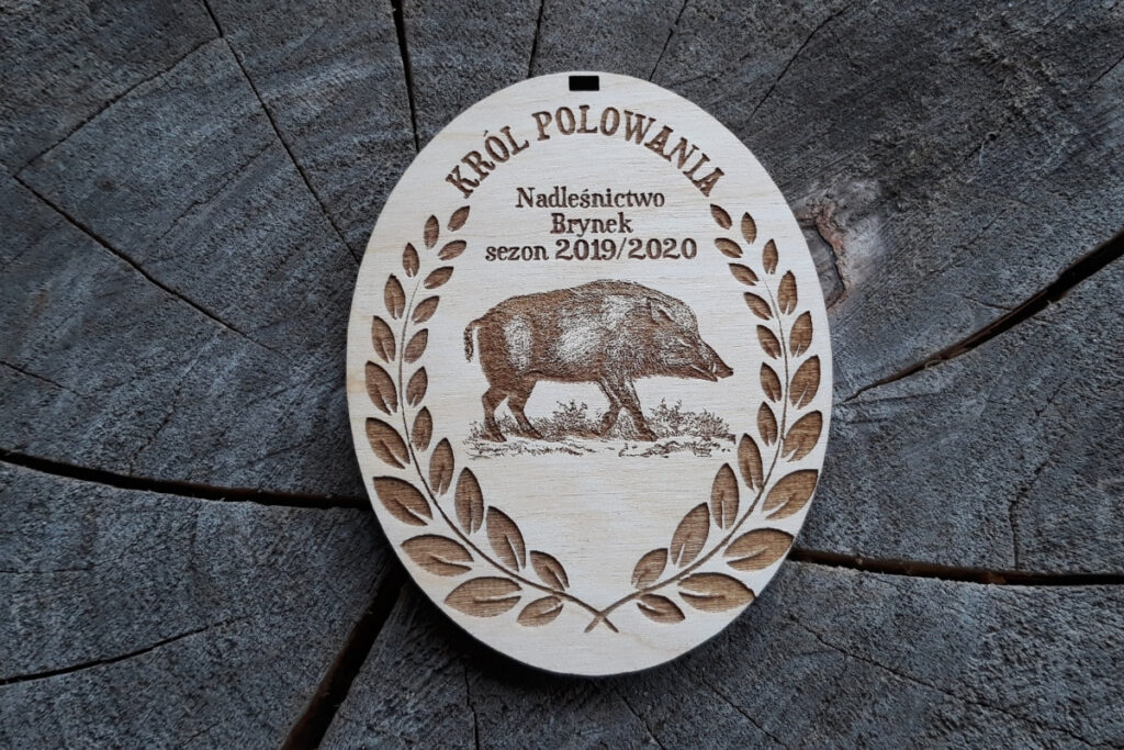 Owalny medal z drewna z grawerem dzika (odyńca) w tradycyjnym wieńcu, z napisem Król Polowania.