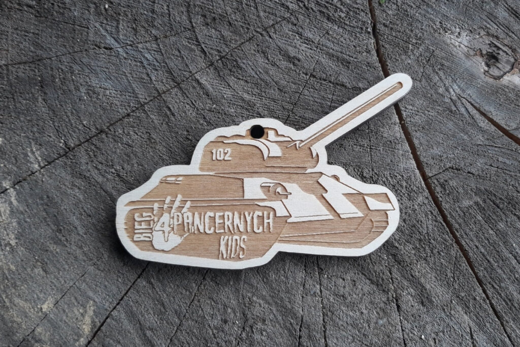 Drewniany medal wycięty w kształcie czołgu z grawerem kół, gąsienic i napisem Bieg 4 Pancernych Kids.
