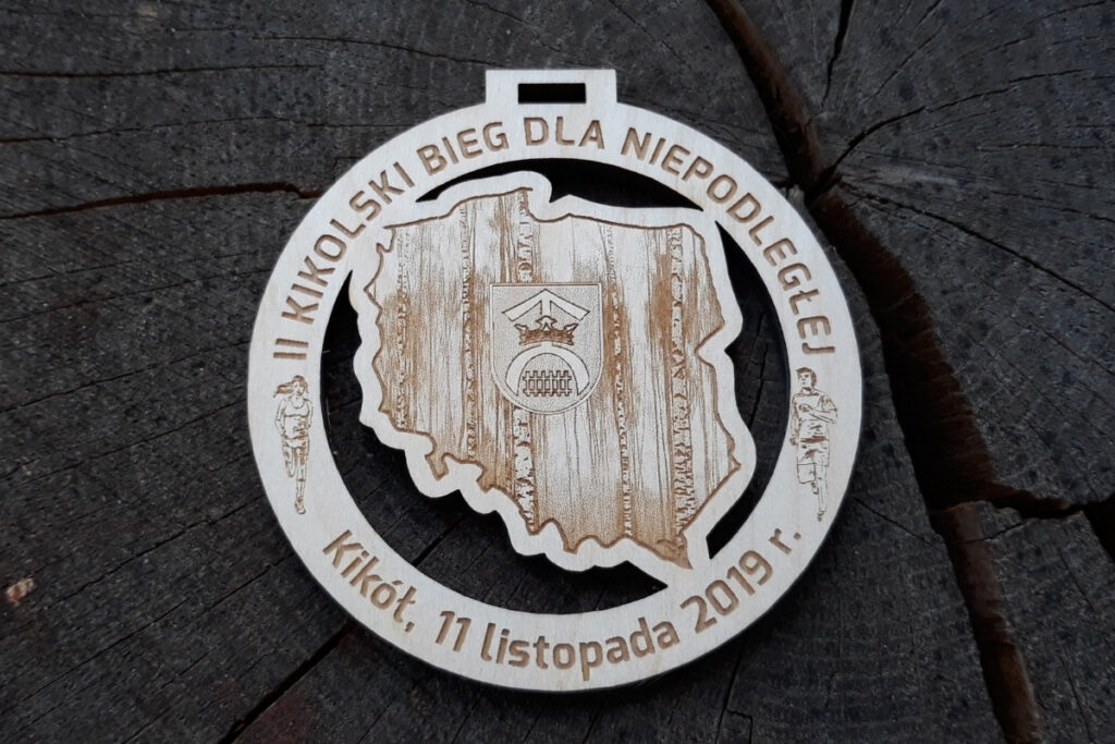 Okrągły drewniany medal z precyzyjnie wyciętym ażurowym konturem mapy Polski w środku, grawerowanym napisem Bieg dla Niepodległej i datą.
