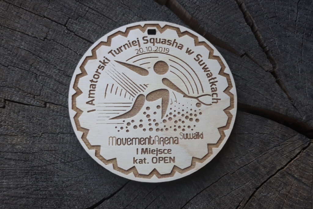 Okrągły drewniany medal do squasha z grawerem rakiety, charakterystycznej piłeczki z dwiema kropkami i gracza oraz napisami.