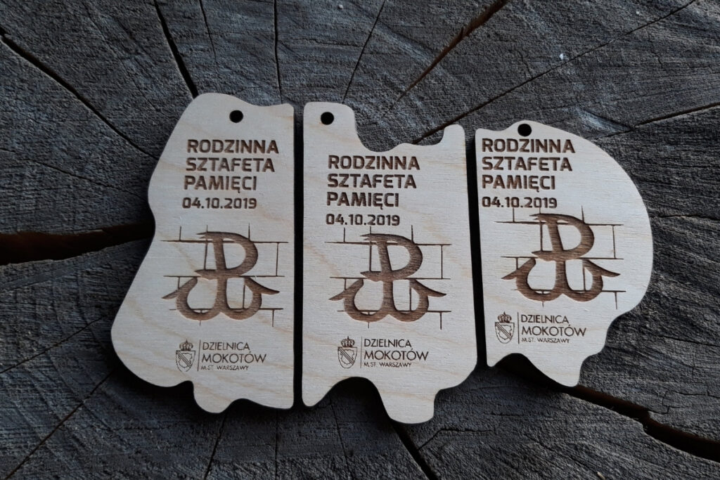 Zestaw trzech drewnianych medali o nieregularnych kształtach, które po złożeniu tworzą prostokątną tabliczkę z napisem Sztafeta Pamięci i grafiką kotwicy - Polski Walczącej.