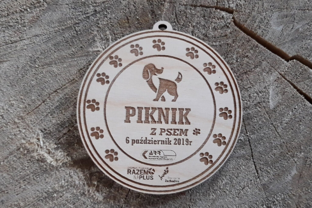 Okrągły drewniany medal z grawerem psich orz napisem Piknik z Psem.