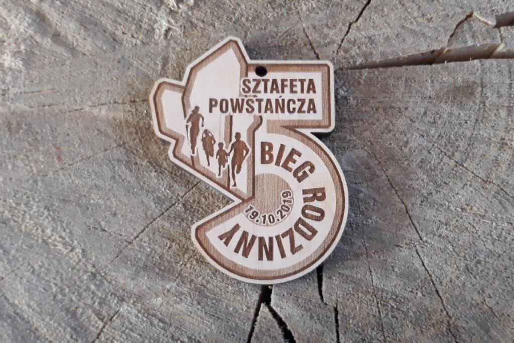 rewniany medal wycięty w kształcie dużej cyfry 5 z grawerem napisu Sztafeta Powstańcza i motywem biegnącej rodziny.