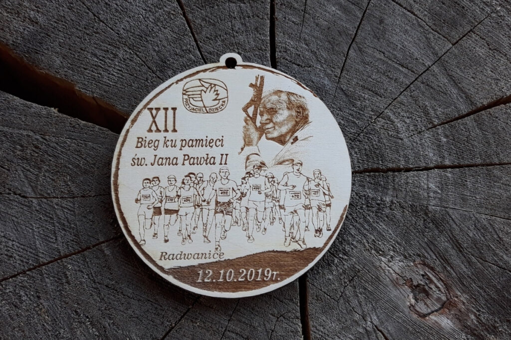 Okrągły drewniany medal z grawerem profilu Jana Pawła II, napisem Bieg ku Pamięci Jana Pawła II i biegaczami.