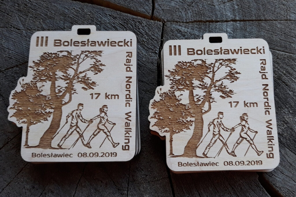 Drewniany medal z grawerem sylwetki maszerującej osoby z kijami Nordic Walking, napisem III Bolesławiecki Rajd i elementami roślinnymi.