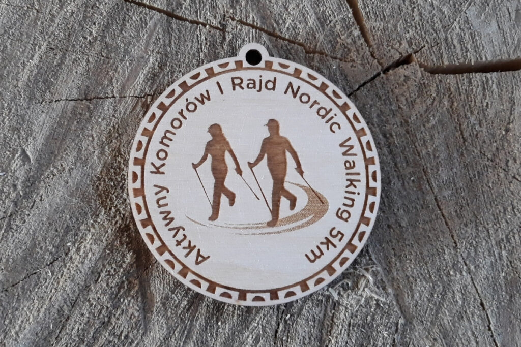 Okrągły drewniany medal z grawerem pary kijkarzy - kobiety i mężczyzny z kijkami idących w marszu Nordic Wslking.