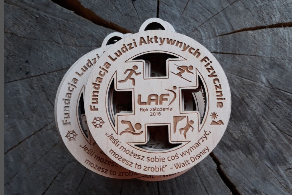 Okrągły drewniany medal z ażurowymi wycięciami, logiem cytatem.