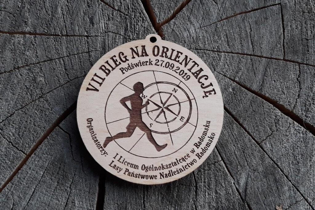 Okrągły drewniany medal z grawerem biegacza, kierunków świata, wykonany z jasnej sklejki - brzozy.