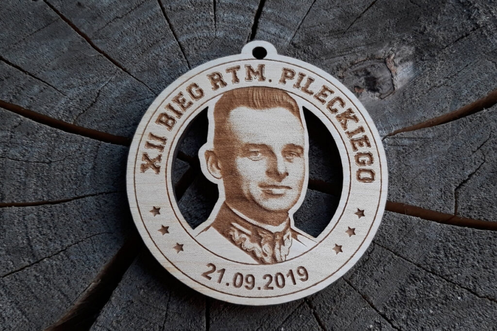 Okrągły drewniany medal z grawerowanym realistycznym portretem Witolda Pileckiego, napisem XII Bieg Rotmistrza Pileckiego i datą wydarzenia.