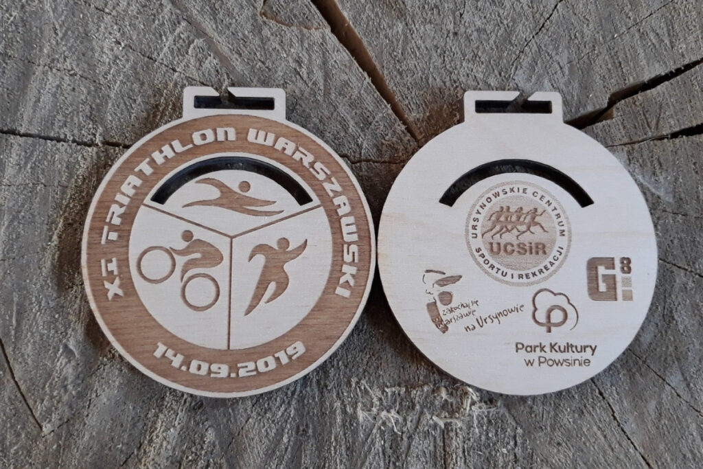 Okrągły drewniany medal z grawerem trzech ikon triathlonu: pływaka, kolarza i biegacza, napisem Triathlon Warszawski.
