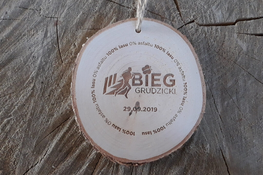 Medal wykonany z naturalnego plastra brzozy z korą, z grawerem logotypu Biegu Grudzickiego i napisem 2019.