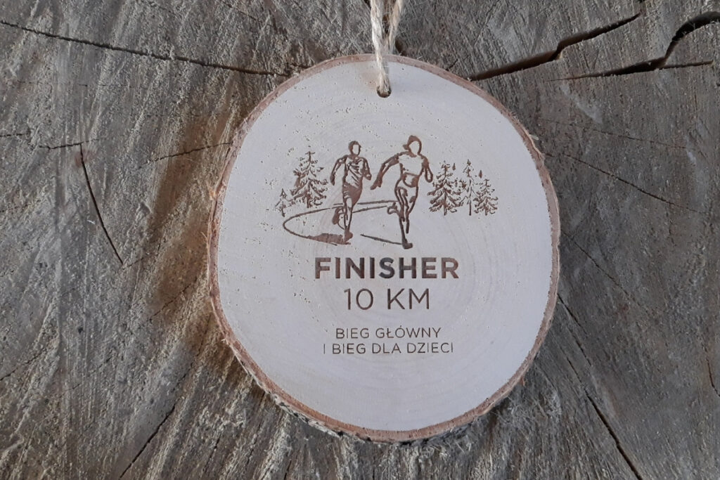 Medal z naturalnego plastra brzozy z korą, z grawerem buta biegowego, napisem Finisher, dystansem 10 km i ozdobnymi gałązkami.