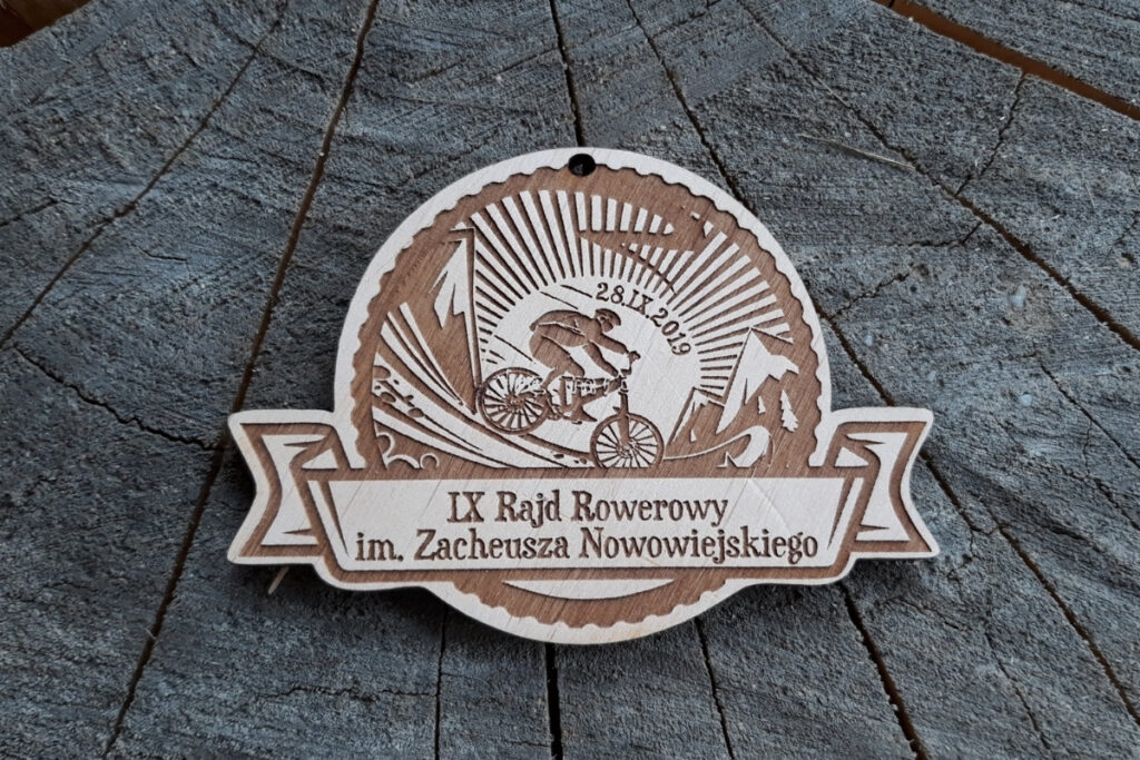 Medal z jasnej płyty brzozowej z precyzyjnym grawerem elementów kojarzących się z rowerami, napisem Rajd Rowerowy i dekoracjami.