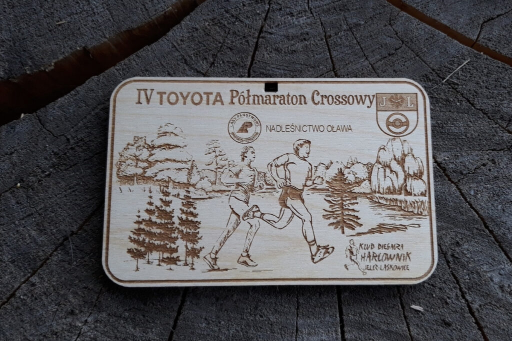 Medal na półmaraton crossowy z drewna, biegacze na tle drzew, u góry napis IV Toyota Półmaraton Crossowy i logo Nadleśnictwa Oława.