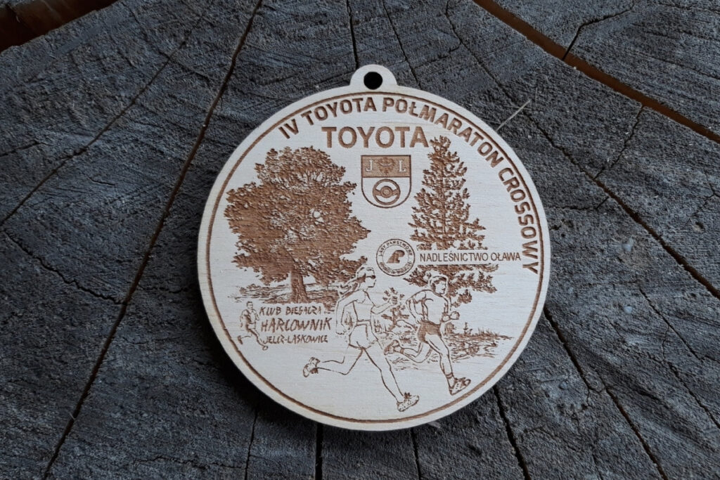 Okrągły drewniany medal z logo Toyota, napisem IV Toyota Półmaraton Crossowy, grafiką biegnącego zawodnika, rokiem wydarzenia i logotypami.