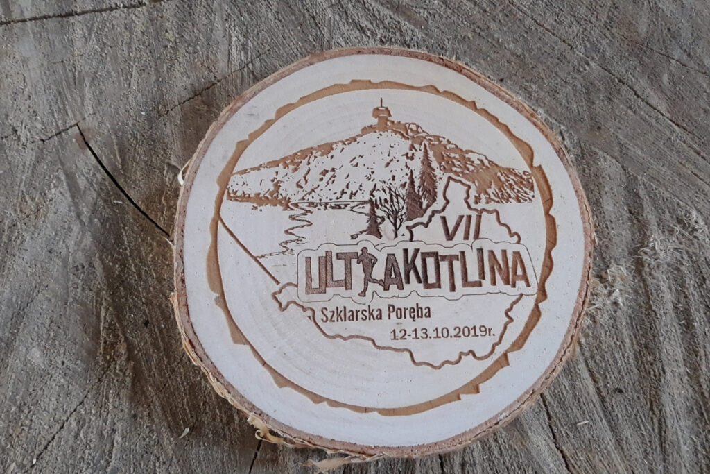 Medal z naturalnego plastra brzozy z korą, z grawerem logotypu Ultrakotlina, grafiką karkonoskich szczytów i dystansem biegu.
