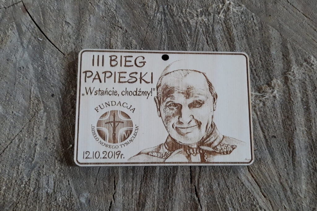 Prostokątny drewniany medal z realistycznym grawerem portretowym św. Jana Pawła II, napisem III Bieg Papieski i datą wydarzenia.