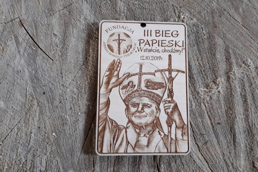 Prostokątny drewniany medal z realistycznym grawerem portretowym św. Jana Pawła II, napisem III Bieg Papieski i datą wydarzenia.