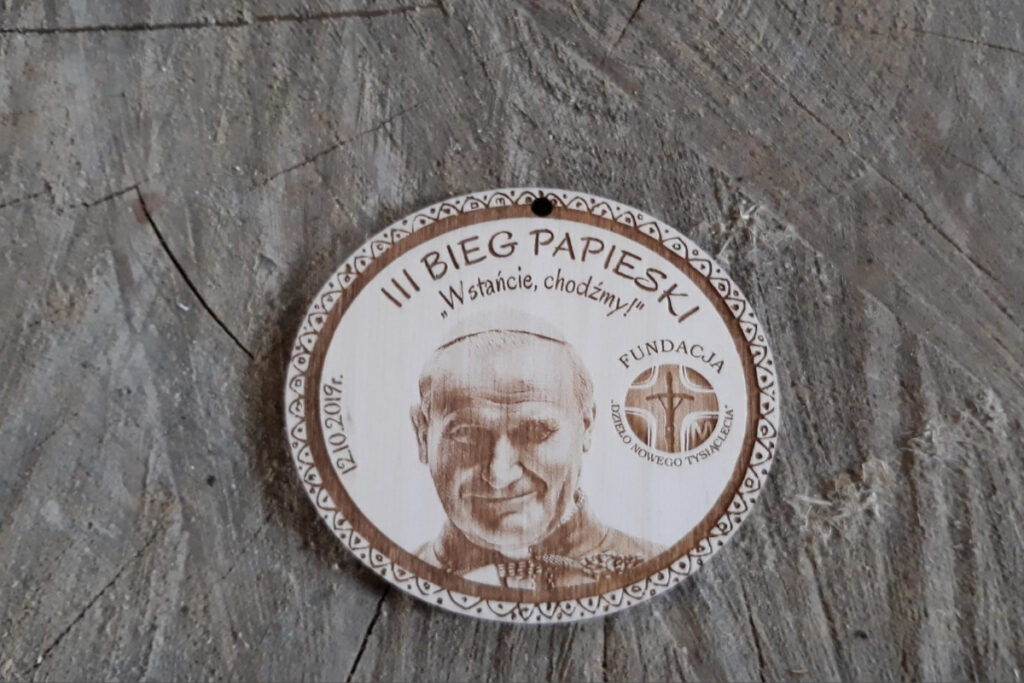 Owalny drewniany medal z realistycznym grawerem portretowym św. Jana Pawła II, napisem III Bieg Papieski i datą wydarzenia.