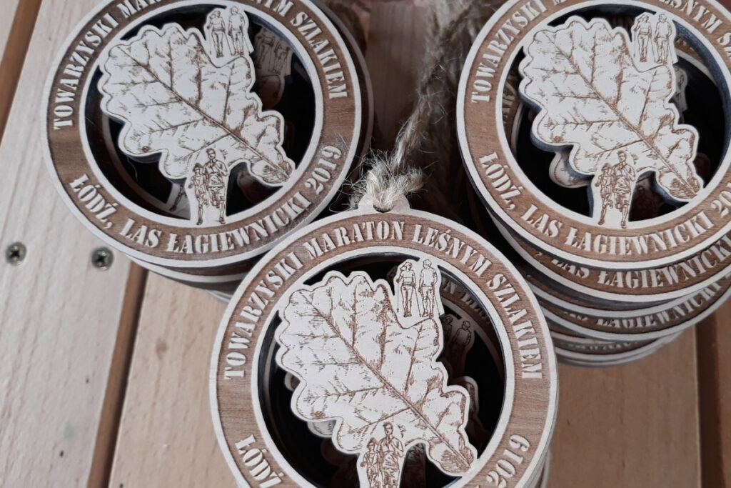 Okrągły drewniany medal z ażurowym wycięciem liścia, grawerem sylwetek biegaczy oraz maszerujących osób z kijkami Nordic Walking.