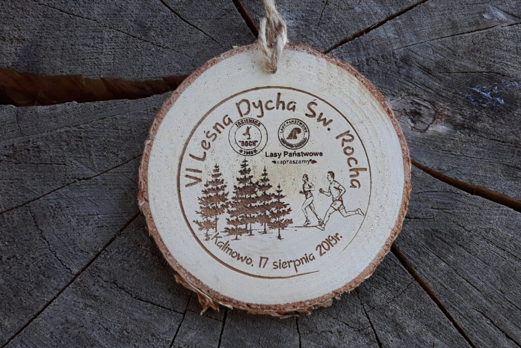 Medal z naturalnego plastra brzozy z korą, z grawerem logotypu Leśna Dycha, sylwetką biegacza na szlaku i rokiem edycji.