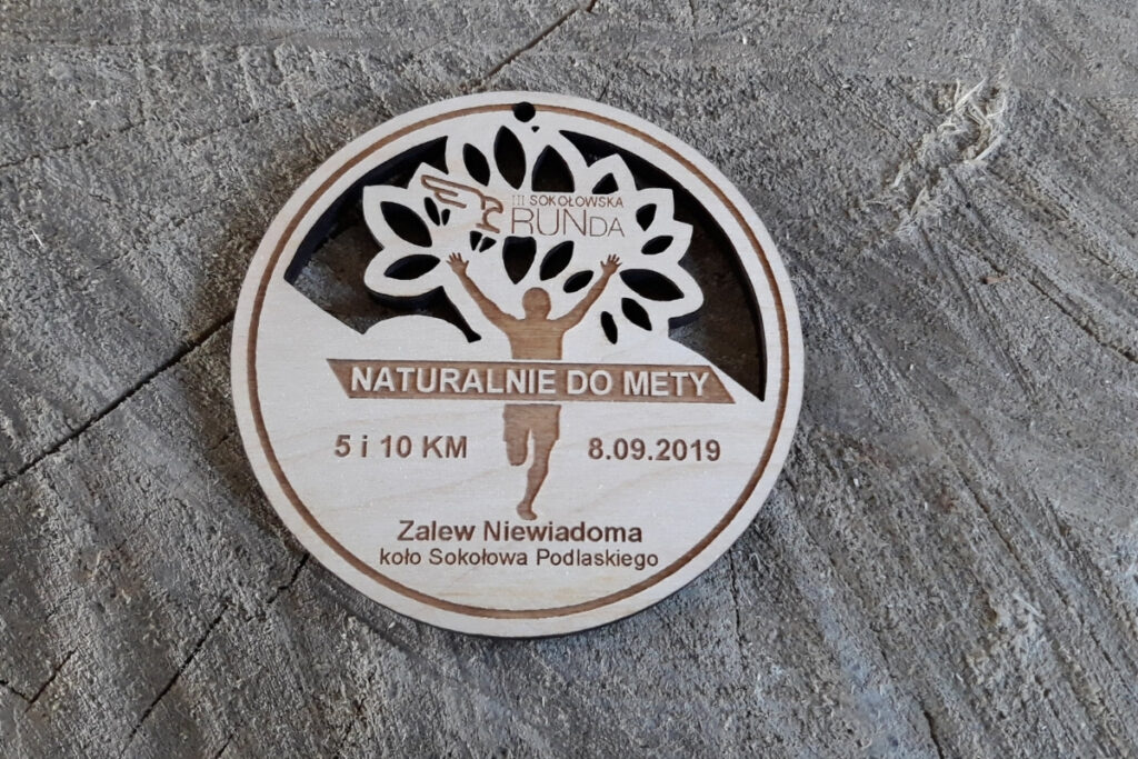 Ażurowy okrągły medal z napisami Sokołowska RUNda i Naturalnie do mety.