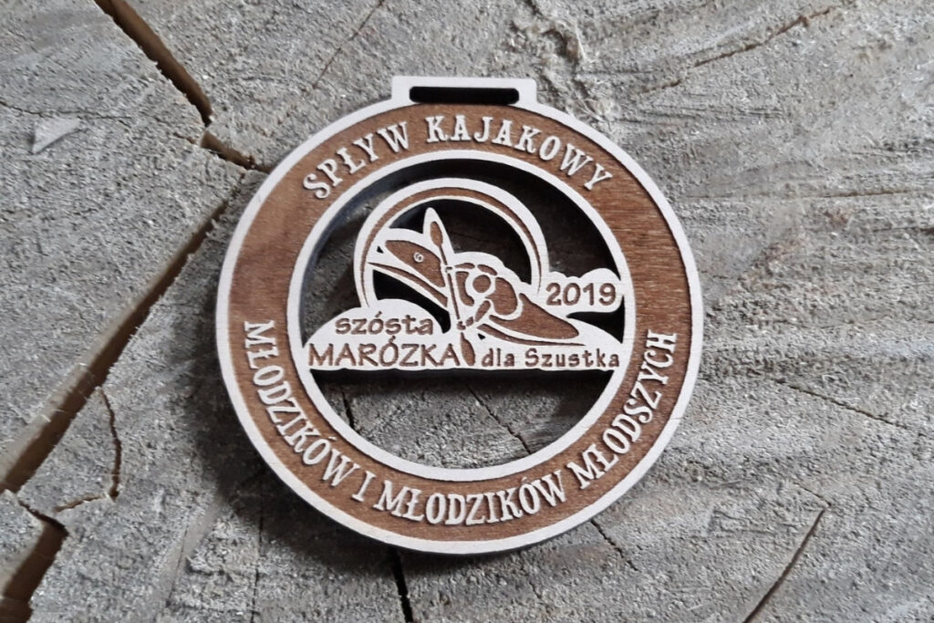 Okrągły drewniany medal z grawerem kajakarza na rzece, napisem Spływ Kajakowy Marózka oraz dedykacją dla ekipy Szustka.
