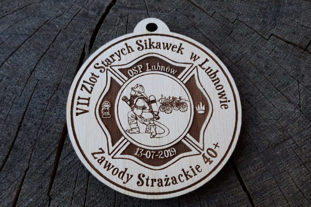 Okrągły drewniany medal z grawerem zabytkowej sikawki konnej, herbem OSP oraz napisem VII Zlot Starych Sikawek Strażackich w Lubnowie.”