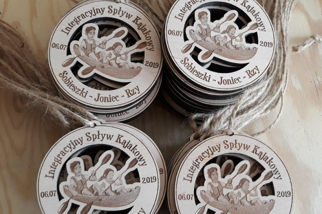 Okrągły drewniany medal z grawerem dwóch kajakarzy w jednym kajaku, napisem Integracyjny Spływ Kajakowy, medal ażurowy.