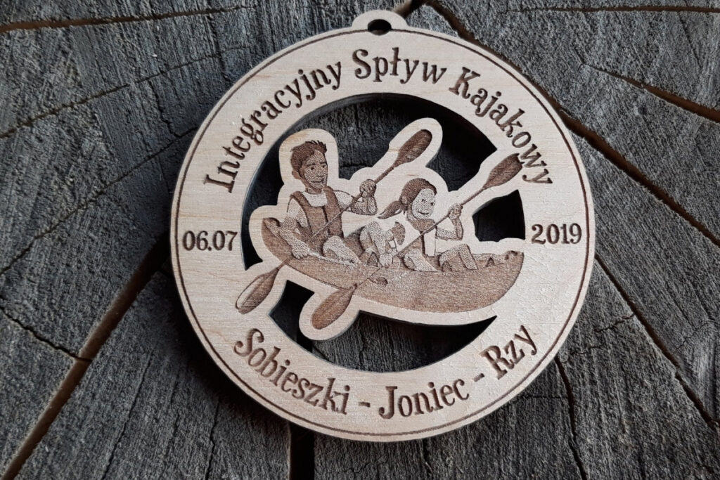 Okrągły drewniany medal z grawerem dwóch kajakarzy w jednym kajaku, napisem Integracyjny Spływ Kajakowy, medal ażurowy.
